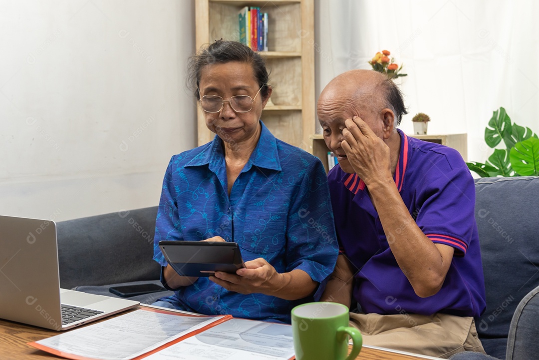 Idosos asiáticos sentam e seguram calculadora para seguro ou despesas médicas e um computador na mesa em casa.
