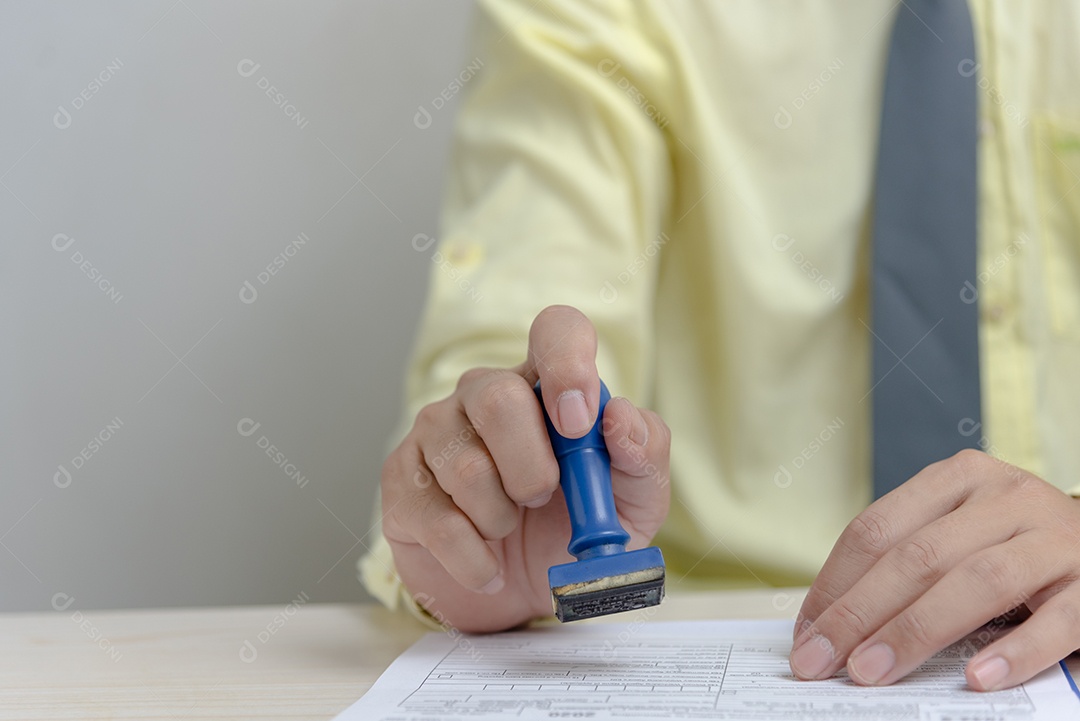 Homem carimbando a aprovação de documentos bancários de finanças de trabalho ou de marketing de investimento na mesa.