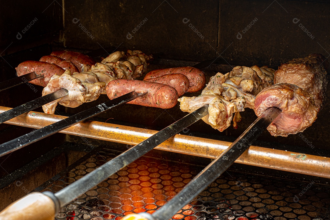 Churrasco sendo preparado na churrasqueira com carvão e fogo quente. Salsicha, carne e frango no espeto