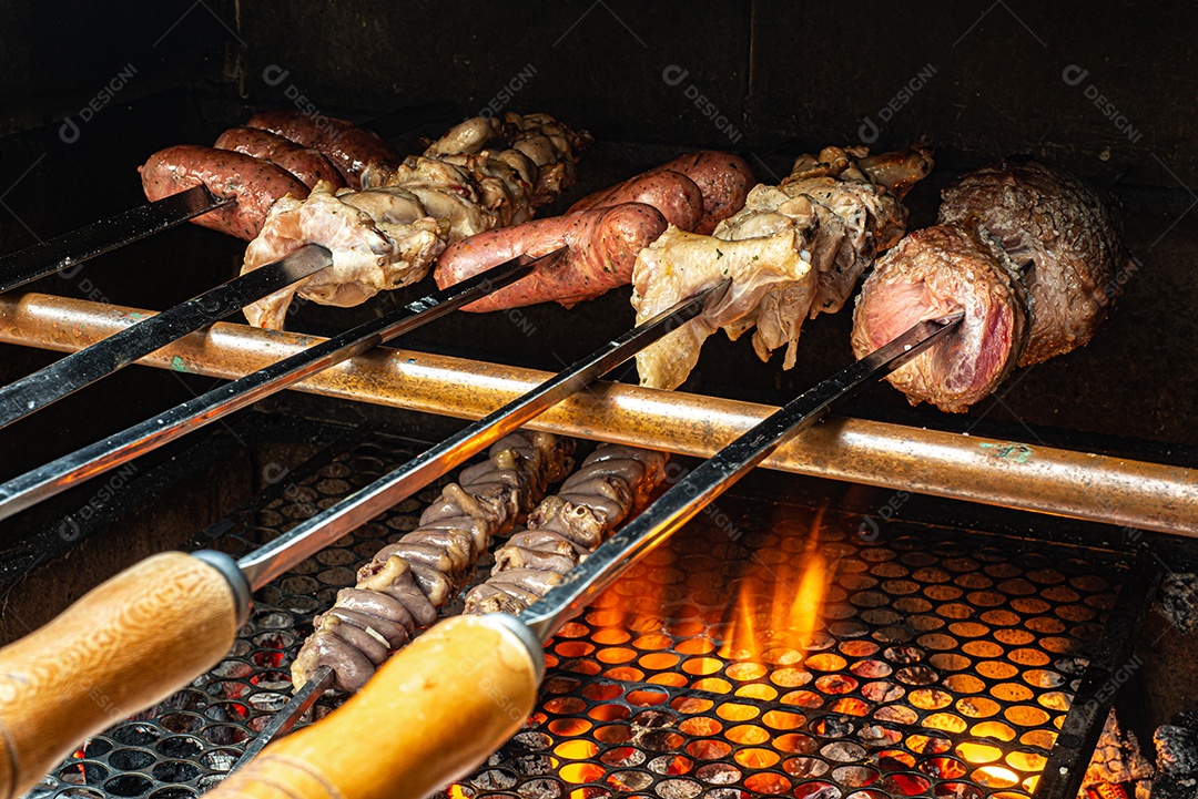 Churrasco sendo preparado na churrasqueira com carvão e fogo quente. Salsicha, carne e frango no espeto