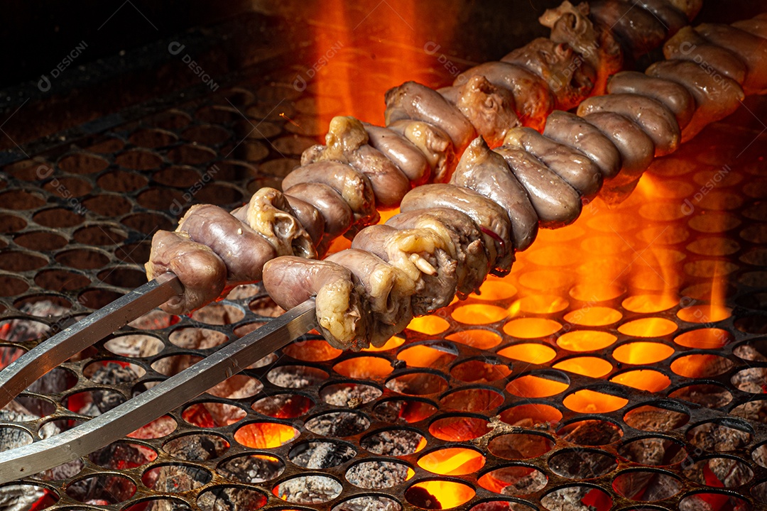 Churrasco sendo preparado na churrasqueira com carvão e fogo quente. Salsicha, carne e frango no espeto