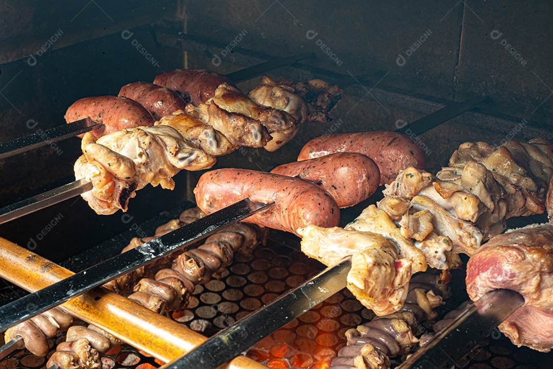 Churrasco sendo preparado na churrasqueira com carvão e fogo quente. Salsicha, carne e frango no espeto