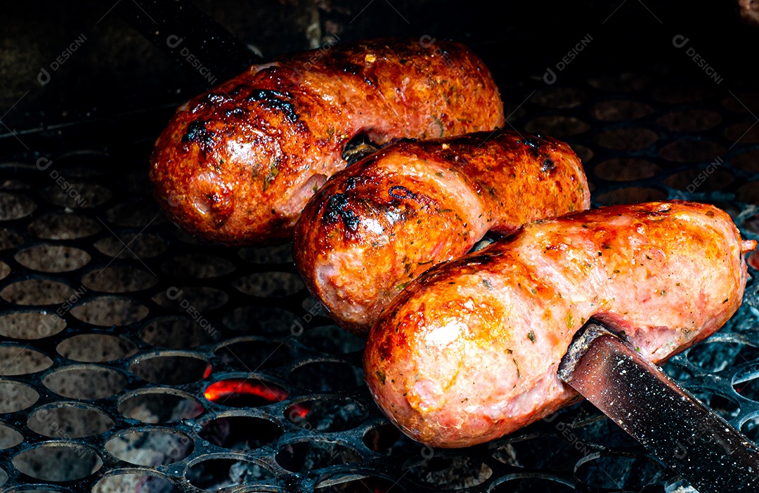 Churrasco sendo preparado na churrasqueira com carvão e fogo quente. linguiça de porco assada no espeto.