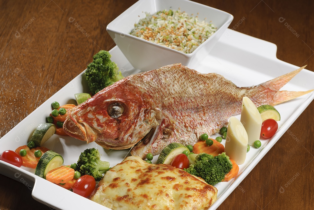 Peixe frito com legumes na mesa de madeira.