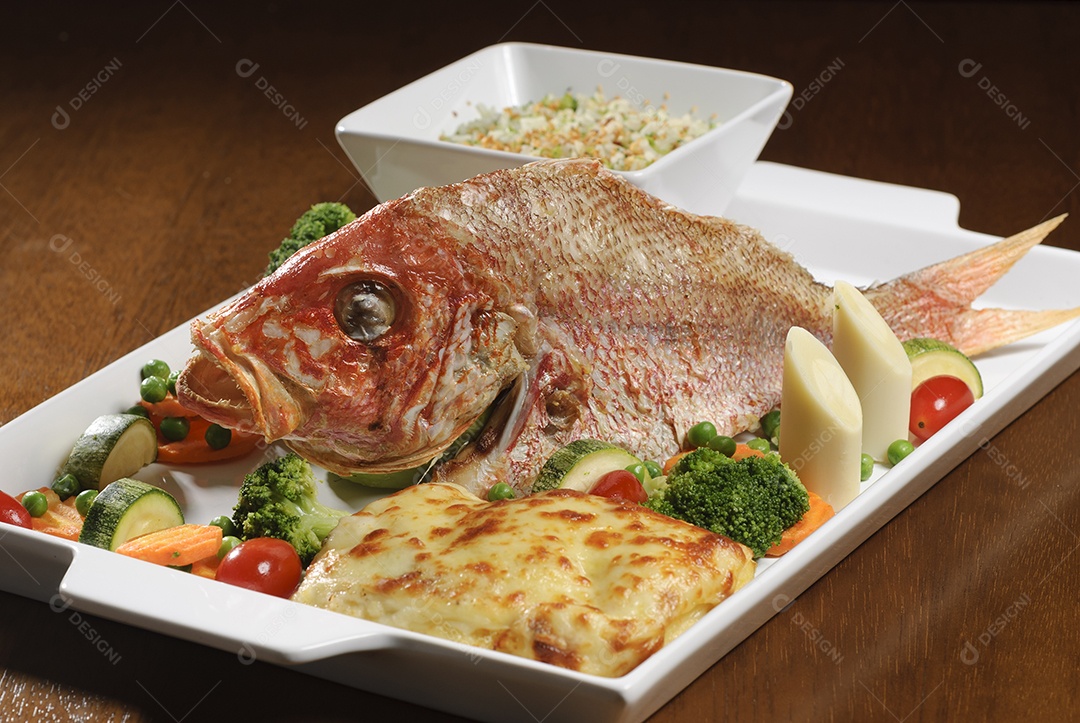 Peixe frito com legumes na mesa de madeira.