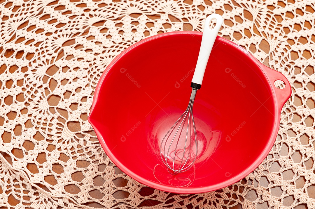 Tigela de plástico vermelha vazia com batedor de ovos. Fundo de toalha de mesa de crochê. Vista do topo. Copie o espaço.