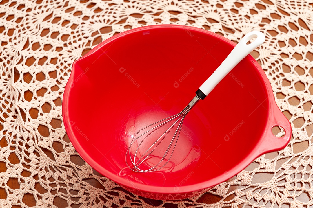 Tigela de plástico vermelha vazia com batedor de ovos. Fundo de toalha de mesa de crochê. Vista do topo. Copie o espaço.