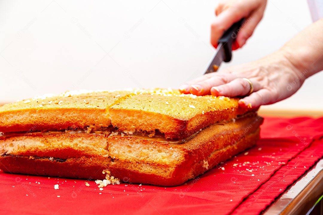 Preparando o bolo - bolo recheado de corte de mão na toalha de mesa vermelha. Isolado no fundo branco. Copie o espaço.