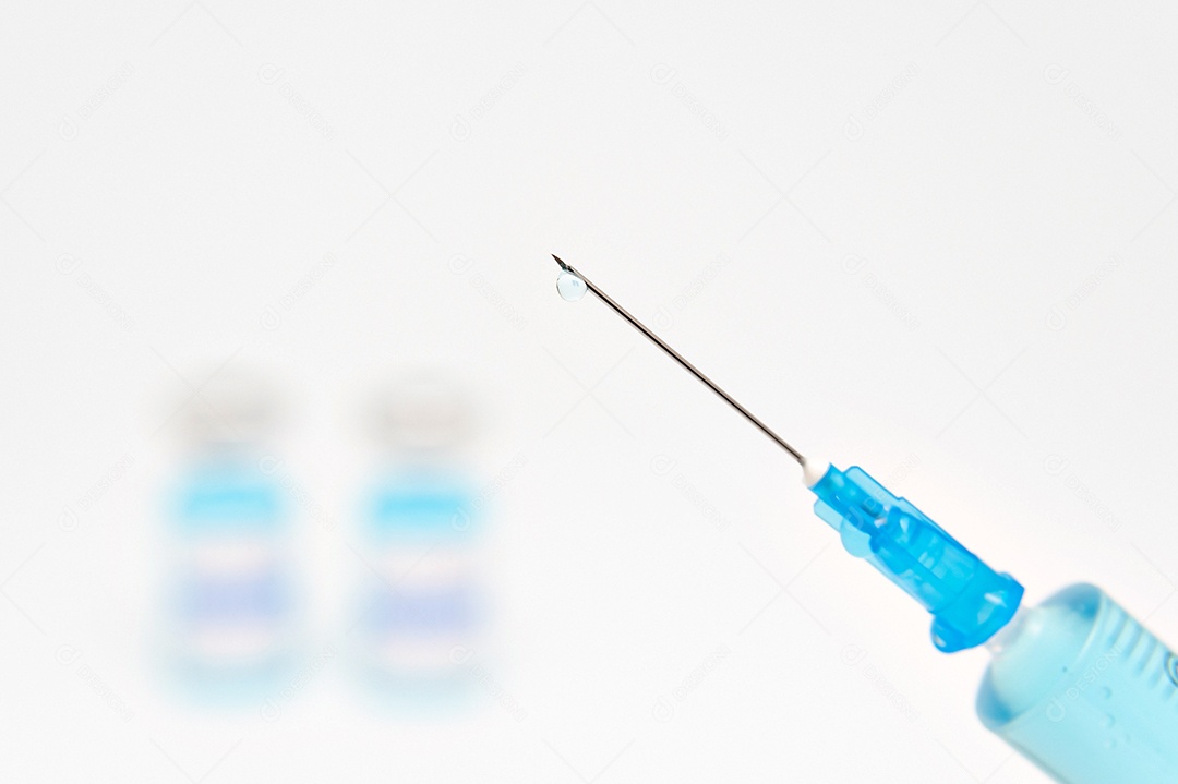 Conceito médico - close-up de seringa com agulha contendo líquido azul. Fundo desfocado com frascos de vacina COVID-19. Isolado no fundo branco.