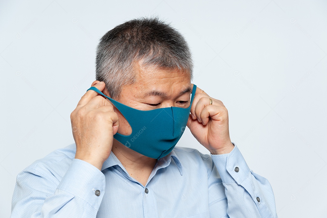 Homem asiático de meia-idade colocando uma máscara facial de poliuretano reutilizável para proteger contra o Covid-19. Isolado no fundo branco.