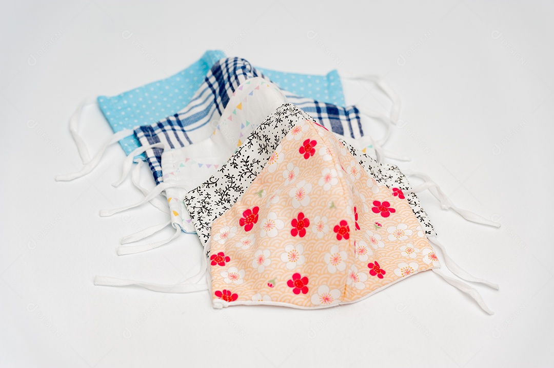 Mão segurando (DIY) máscara de tecido cirúrgico caseiro para proteção contra Coronavirus (COVID-19) e outras doenças infecciosas. Com várias outras máscaras coloridas em fundo branco.