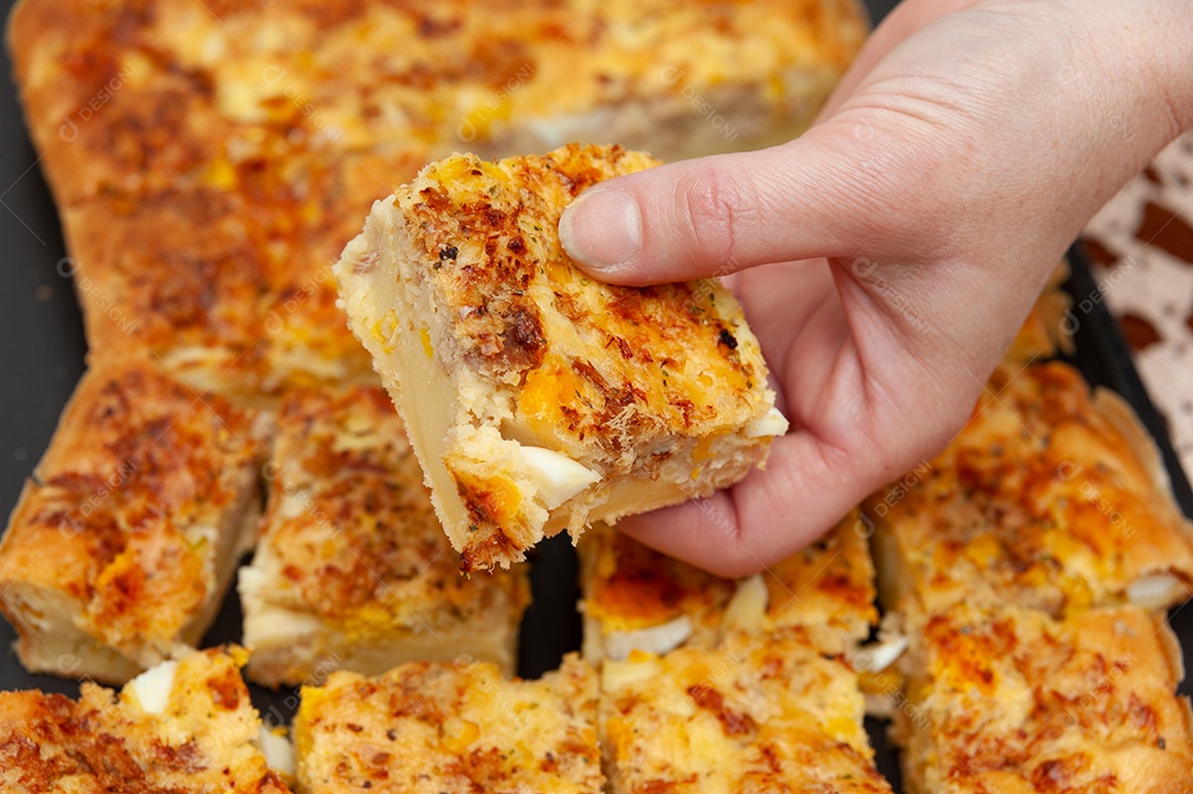 Mãos de mulher pegando um pedaço de Brazilian Blender Savory Pie - Comida tradicional brasileira feita com atum, ovo cozido, milho, frango desfiado, legumes etc.