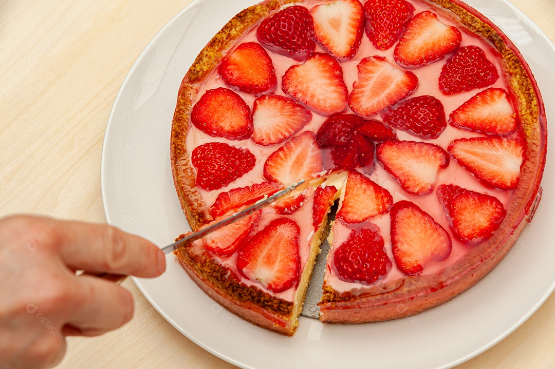 Mão cortando deliciosa torta de morango caseira. Isolado em fundo de madeira. Vista do topo. Fechar-se. Tiro horizontal.