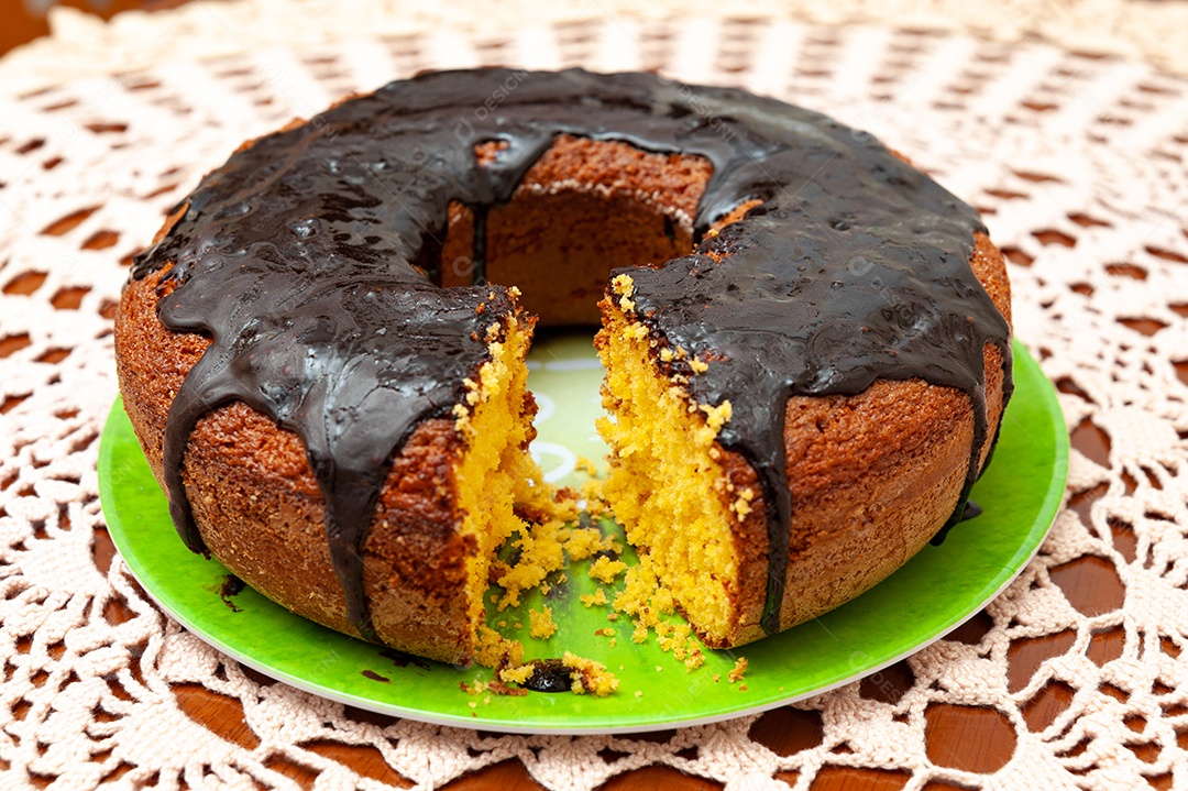 Vista perpendicular do delicioso e saudável bolo de cenoura caseiro tradicional brasileiro com calda de chocolate. Fundo com toalha de crochê.