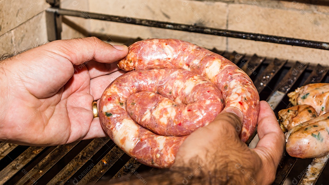 man putting raw sausage on grill, high angle