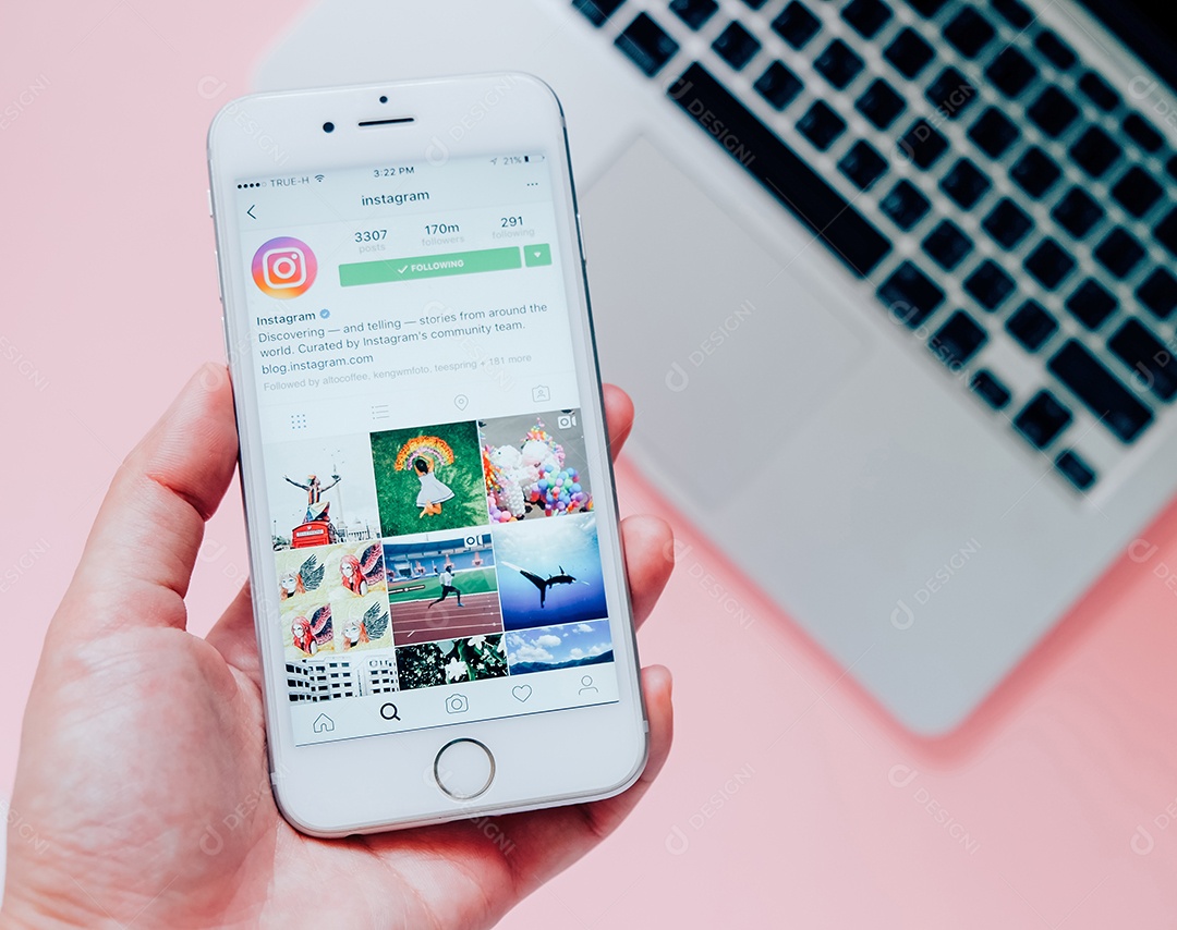 Mão segurando Apple iPhone6s com aplicativo Instagram na tela com fundo de laptop.