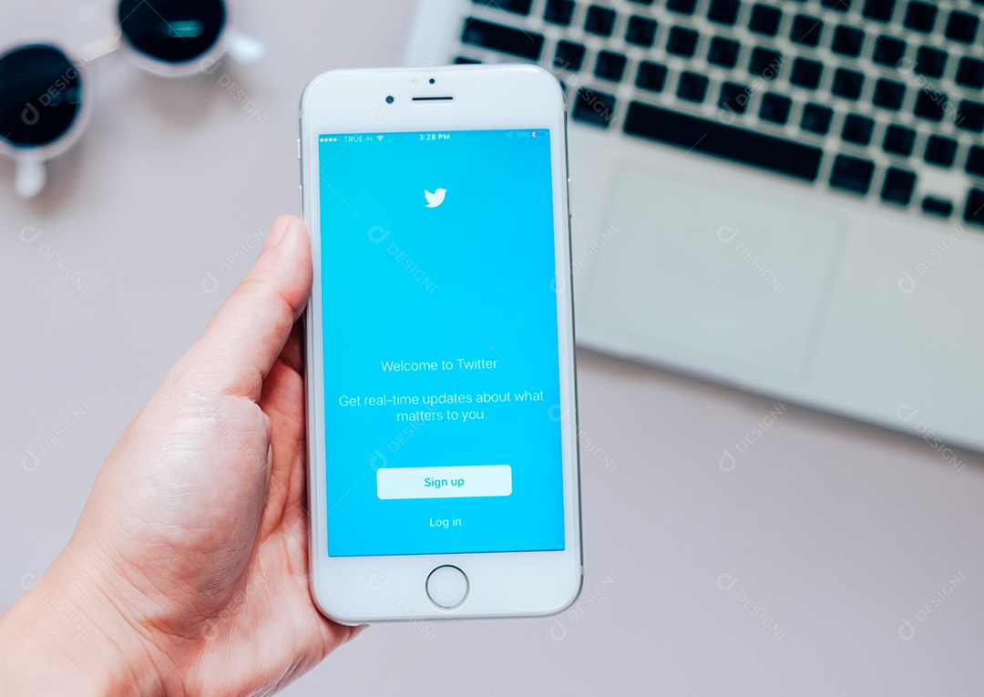 Mão segurando Apple iPhone 6s mostrando inscrição no aplicativo Twitter com laptop
