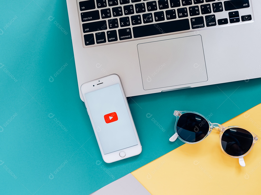 Smartphone com o aplicativo do YouTube na tela do laptop com óculos escuros e fundo colorido