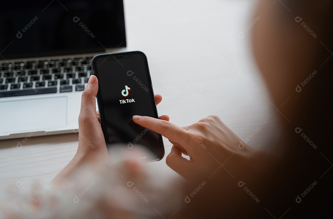 Mulher usando iPhone XS mostrando o aplicativo Tik Tok na tela e laptop