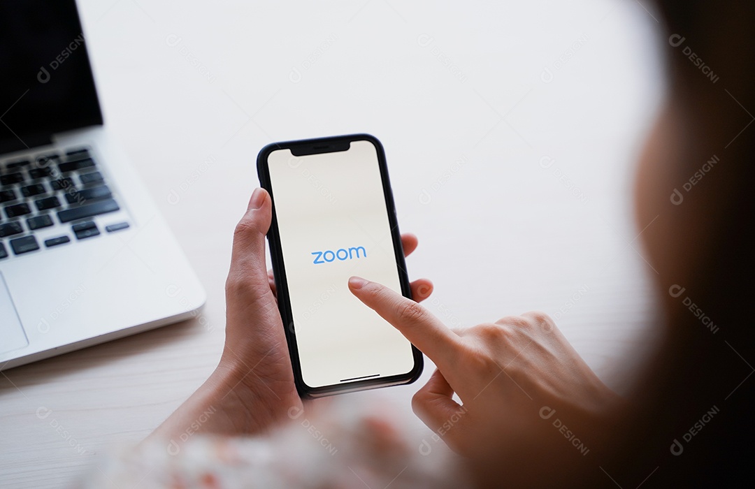 Mulher usando iPhone mostrando aplicativo de zoom e laptop.