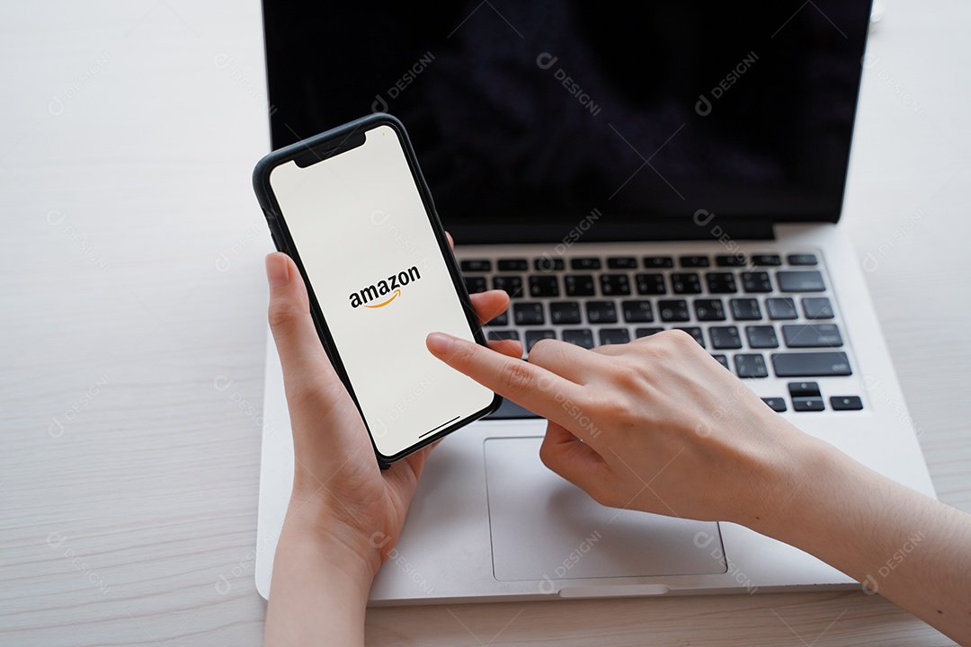 Mulher usando iPhone XS mostrando aplicativo da Amazon na tela e laptop