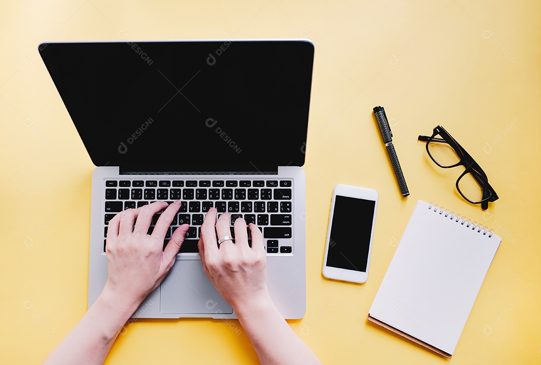 Postura plana da mesa do espaço de trabalho com mãos de mulher digitando no laptop com inteligência