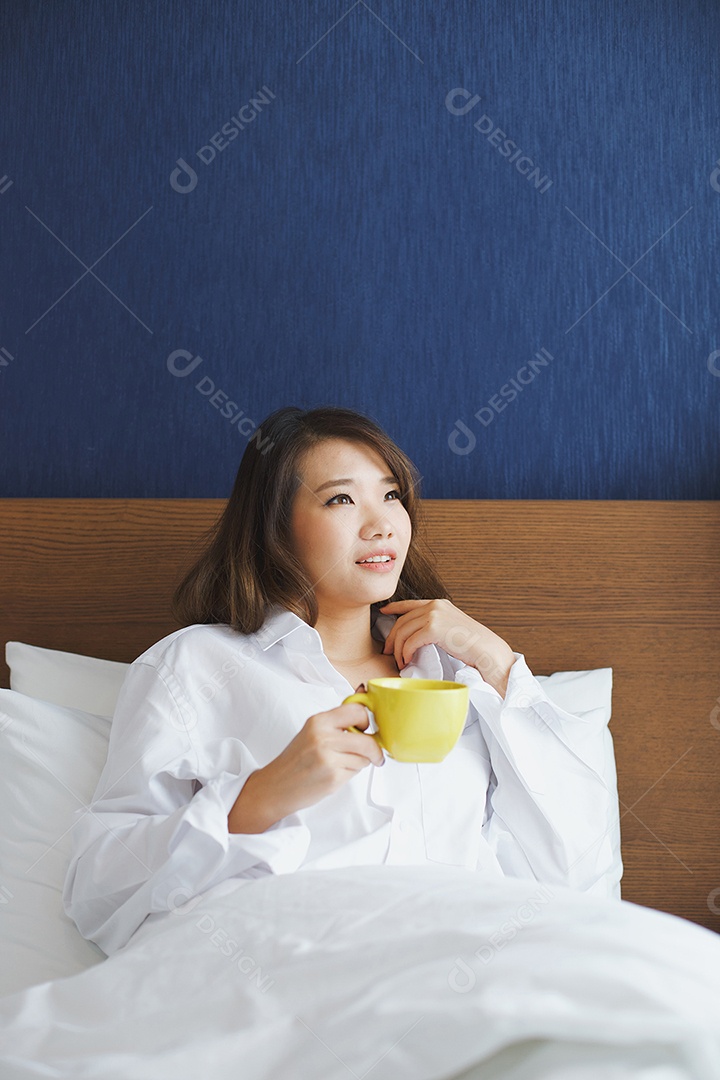 Jovem mulher atraente asiática tomando café na cama