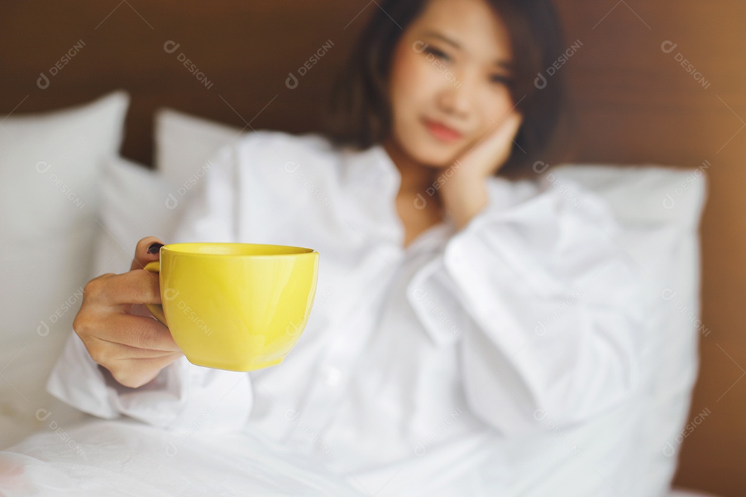 Café da manhã na cama, jovem mulher asiática segurando xícara de café quente