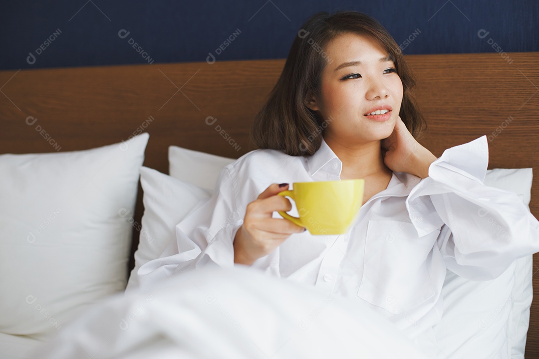 Café da manhã na cama, jovem mulher asiática segurando xícara de café quente
