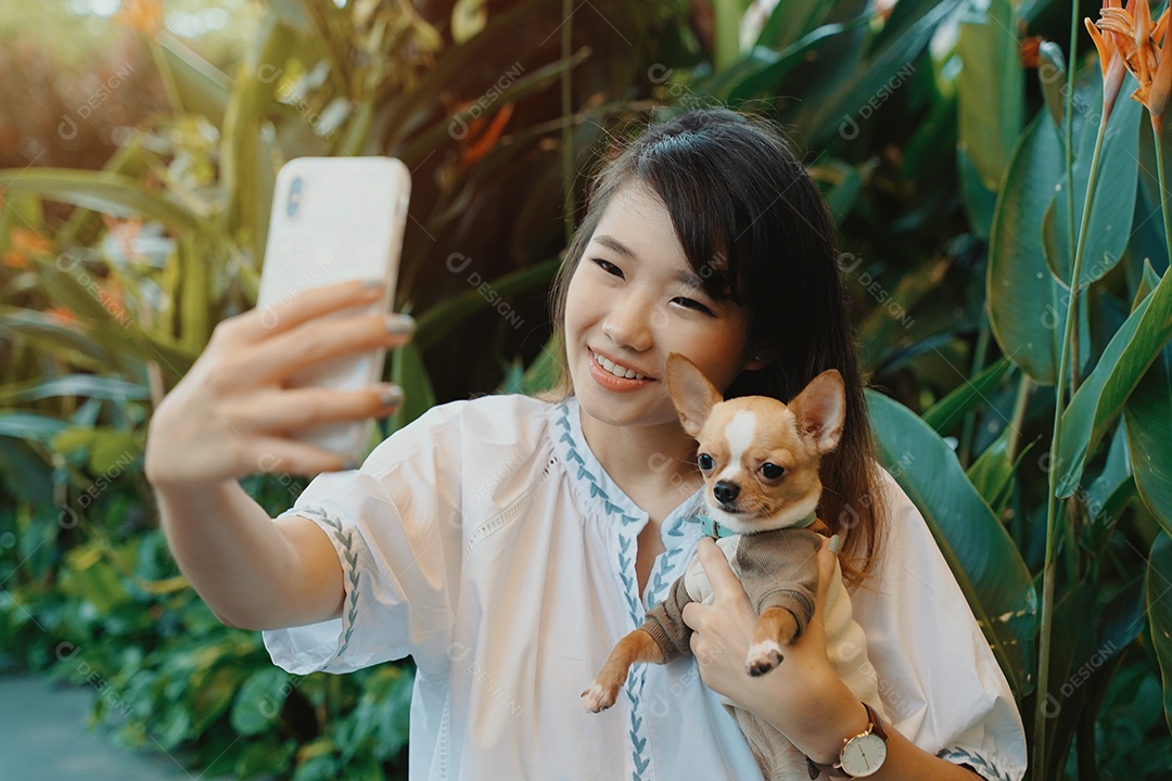 Bonita jovem asiática tirando selfie com seu cachorro chihuahua