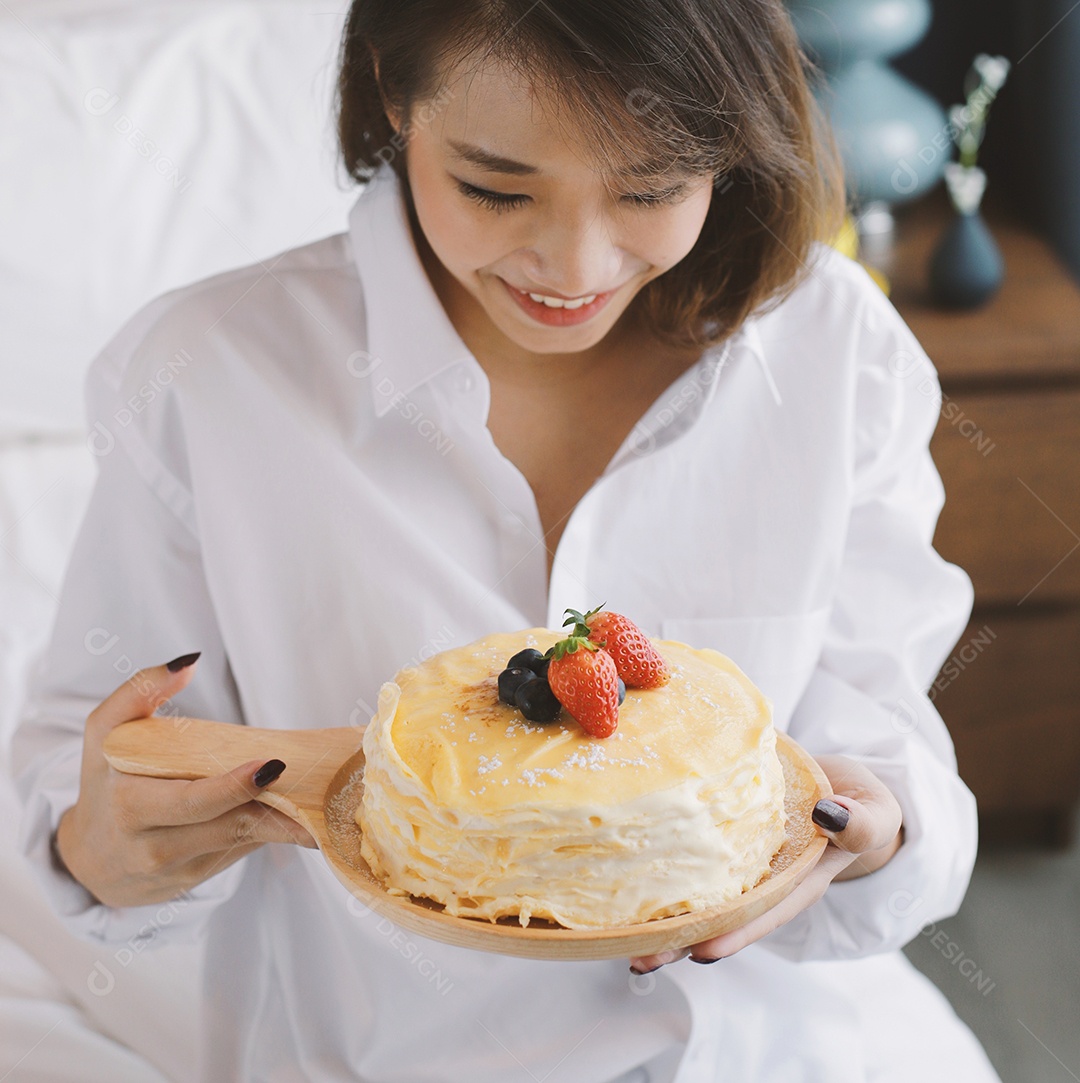 Jovem mulher asiática sorrindo e segurando saboroso bolo de crepe com azul