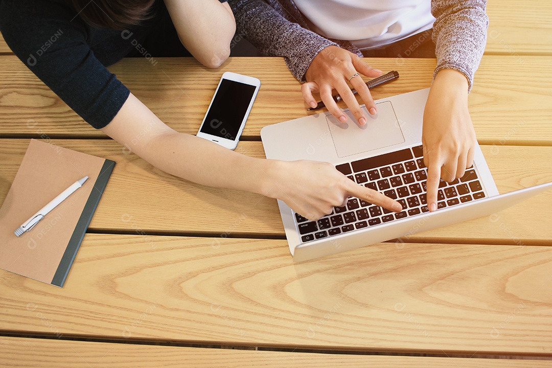 Visão superior de empresárias fazendo brainstorming e usando laptop em madeira