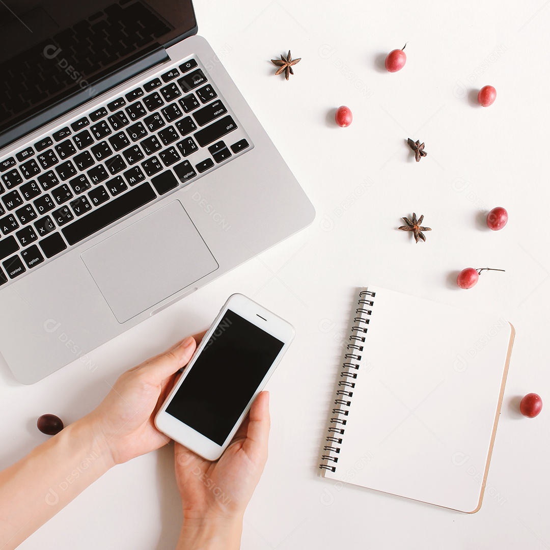 Postura plana de mão segurando smartphone, caderno em branco e laptop