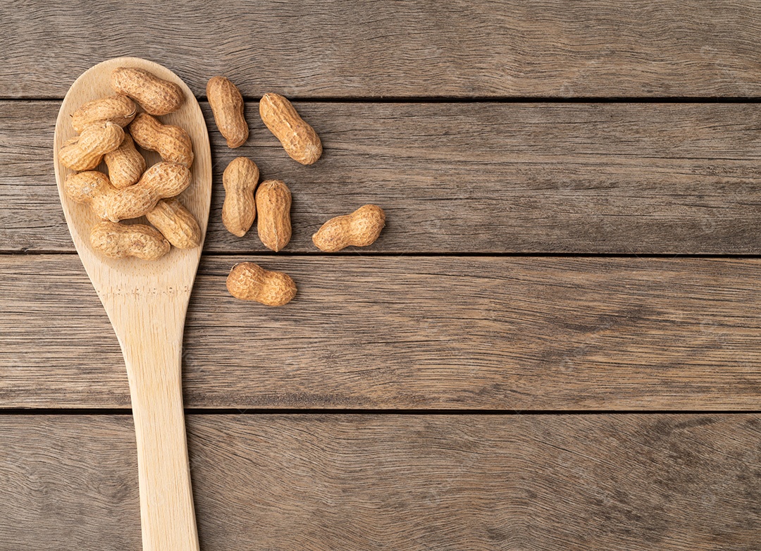 Amendoins sem casca em uma colher sobre a mesa de madeira com espaço de cópia.