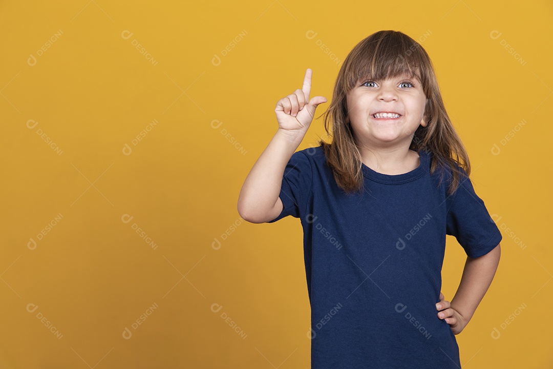 Retrato de menina criança com o dedo apontado para cima. Criança em pose tem ideia isolada no quadro-negro amarelo