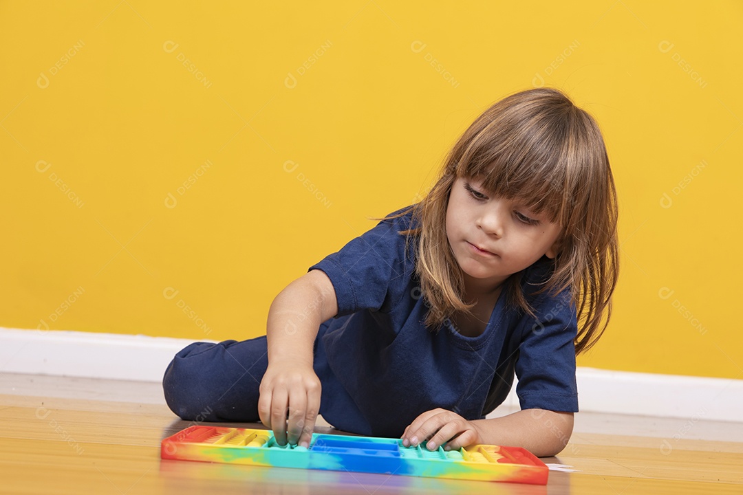 Menina alegre joga em um brinquedo pop de plástico multicolorido Jogando em casa durante as férias de verão