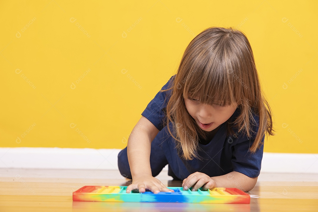 Menina alegre joga em um brinquedo pop de plástico multicolorido Jogando em casa durante as férias de verão