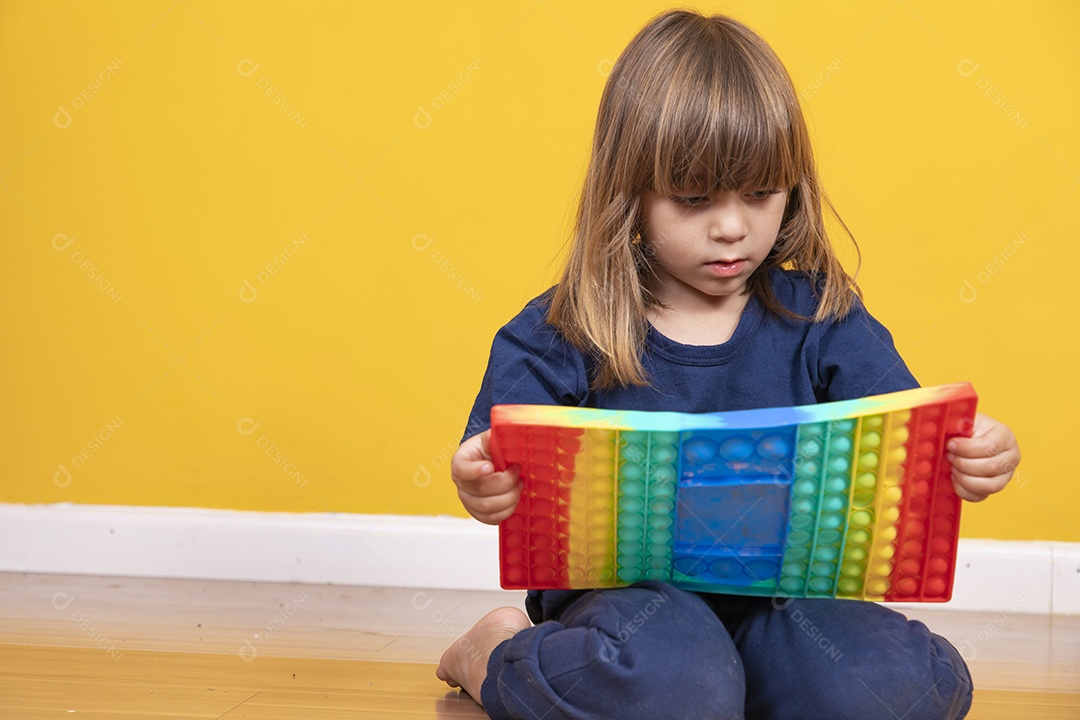 Menina alegre joga em um brinquedo pop de plástico multicolorido Jogando em casa durante as férias de verão