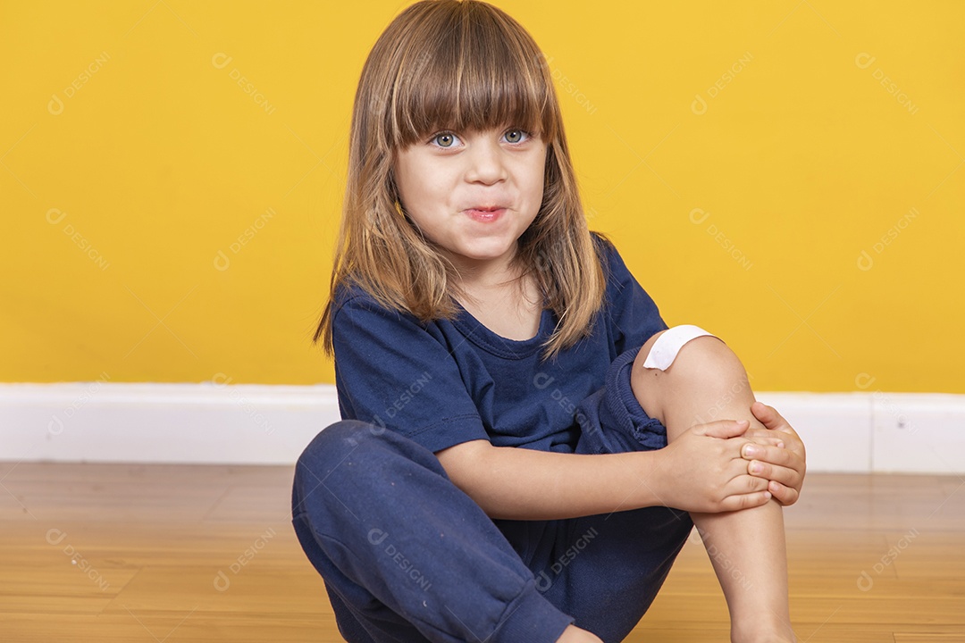 menina sentada no chão com curativo no joelho simulando uma contusão