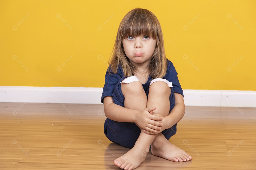 menina sentada no chão com curativo no joelho simulando uma contusão