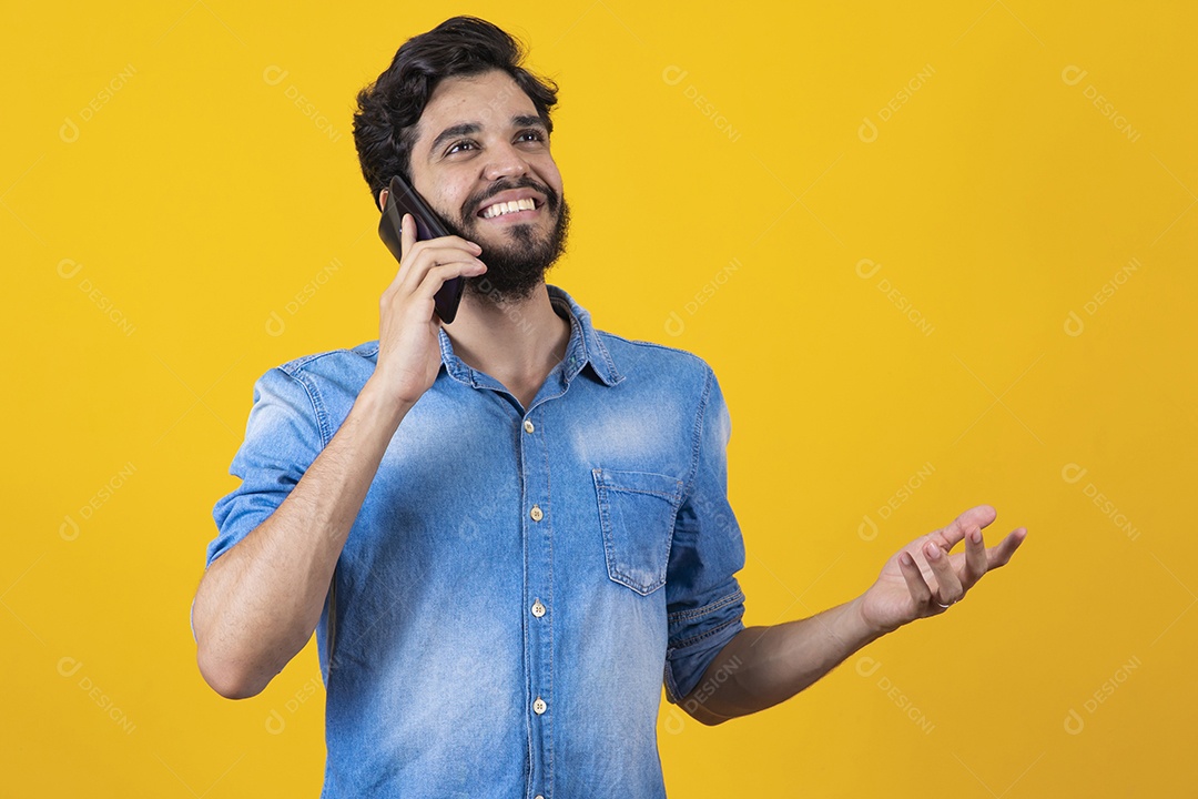 Homem jovem barbudo segurando celular sobre fundo amarelo