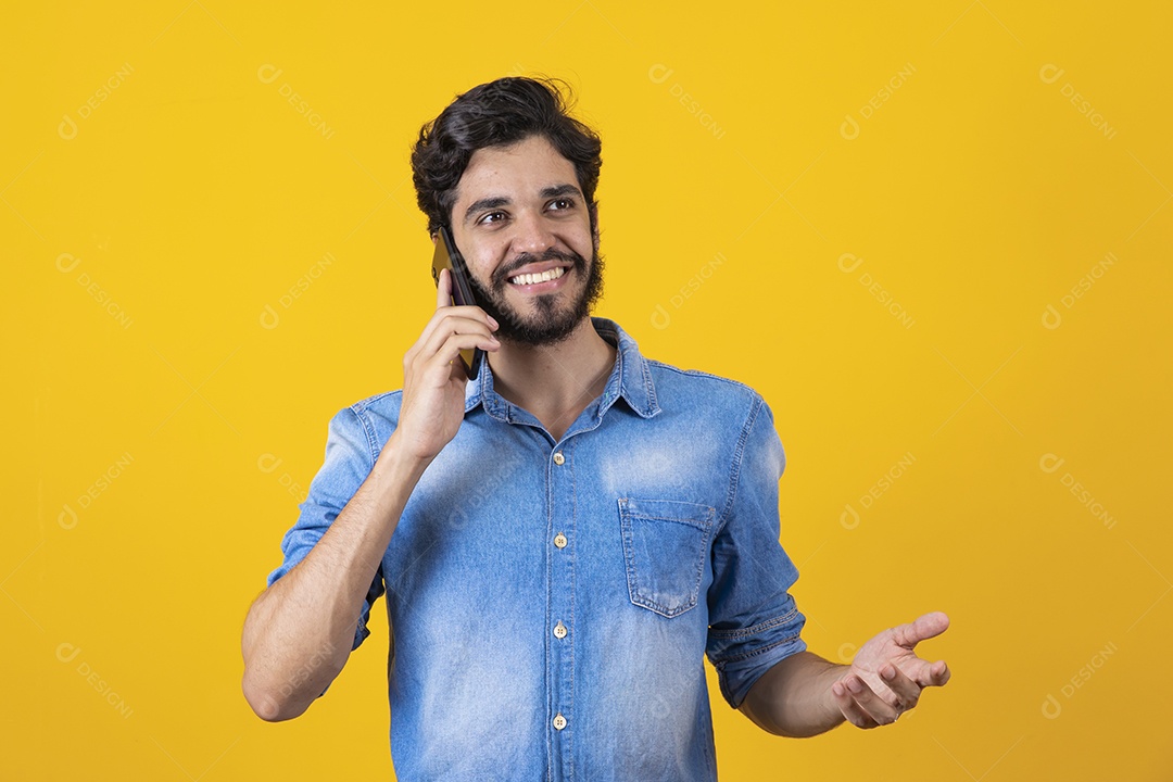 Homem jovem barbudo segurando celular sobre fundo amarelo