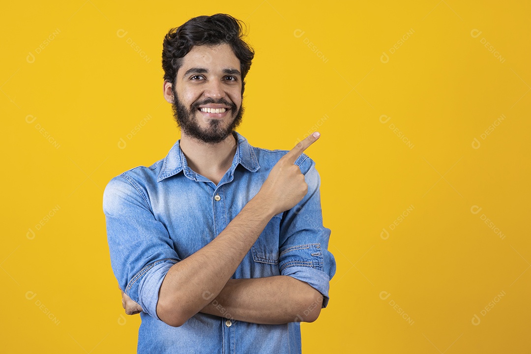 Homem jovem barbudo apontando para o lado sobre fundo amarelo