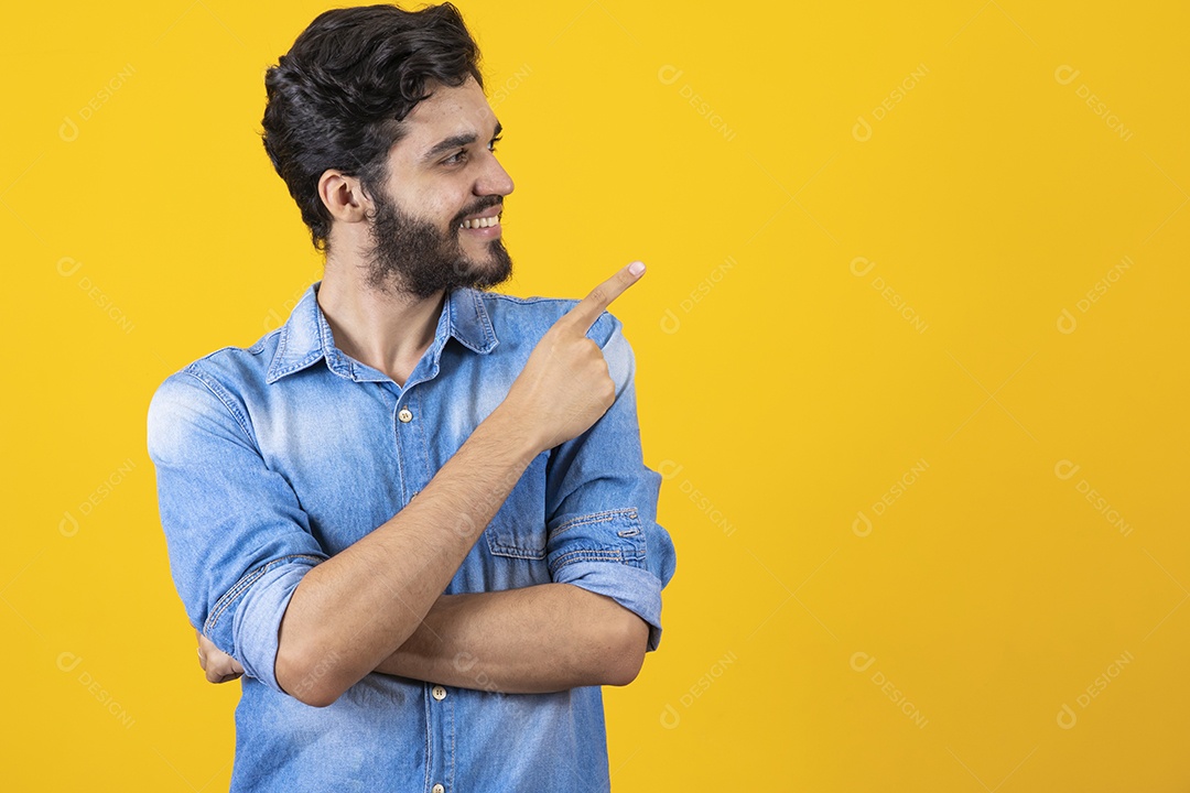 Homem jovem barbudo apontando para o lado sobre fundo amarelo