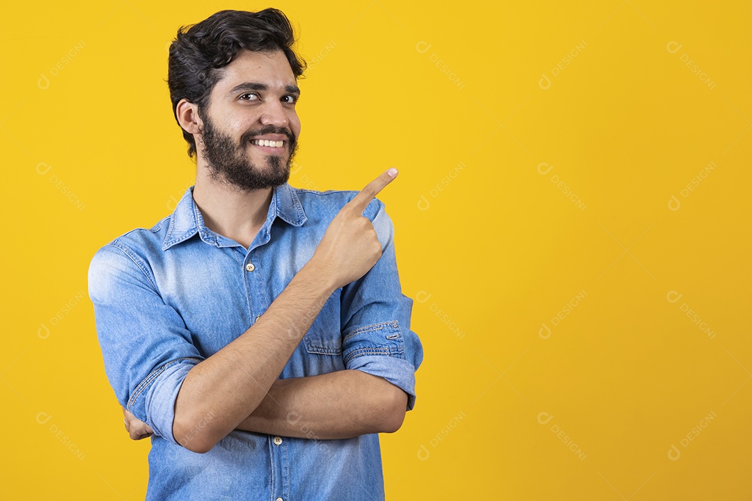 Homem jovem barbudo apontando para o lado sobre fundo amarelo