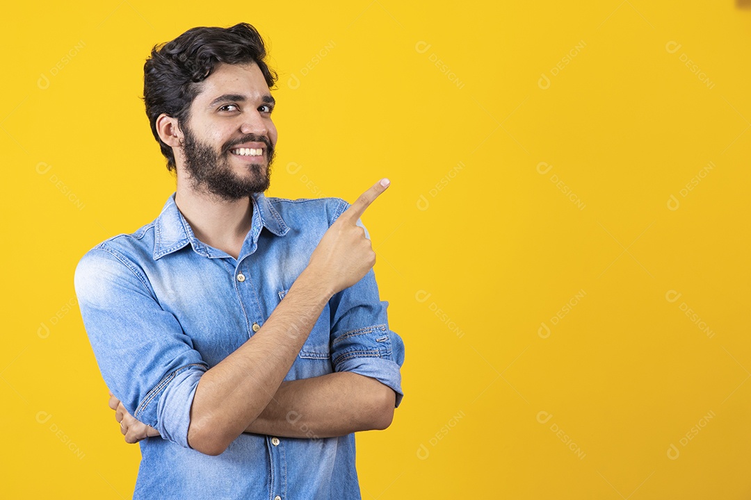Homem jovem barbudo apontando para o lado sobre fundo amarelo