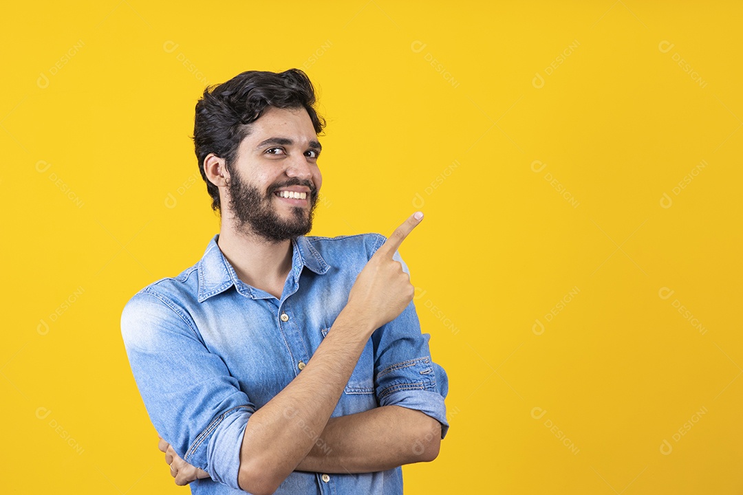 Homem jovem barbudo apontando para o lado sobre fundo amarelo