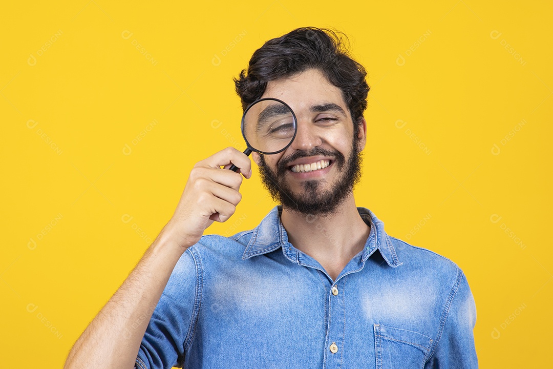 Homem jovem barbudo usando lupa sobre fundo amarelo