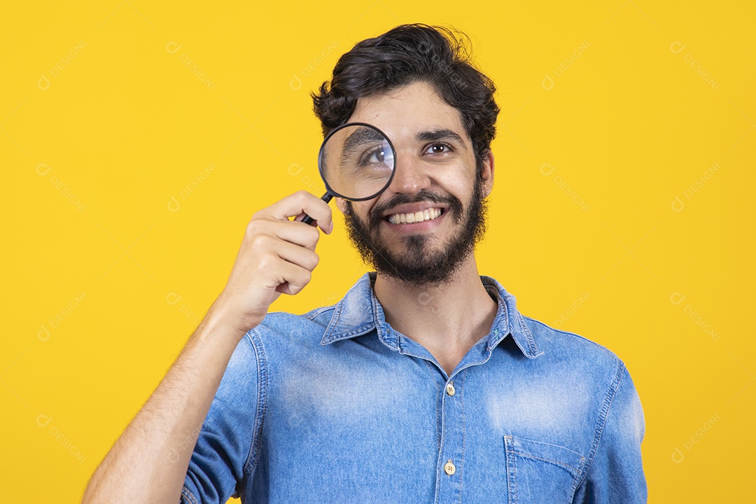 Homem jovem barbudo usando lupa sobre fundo amarelo