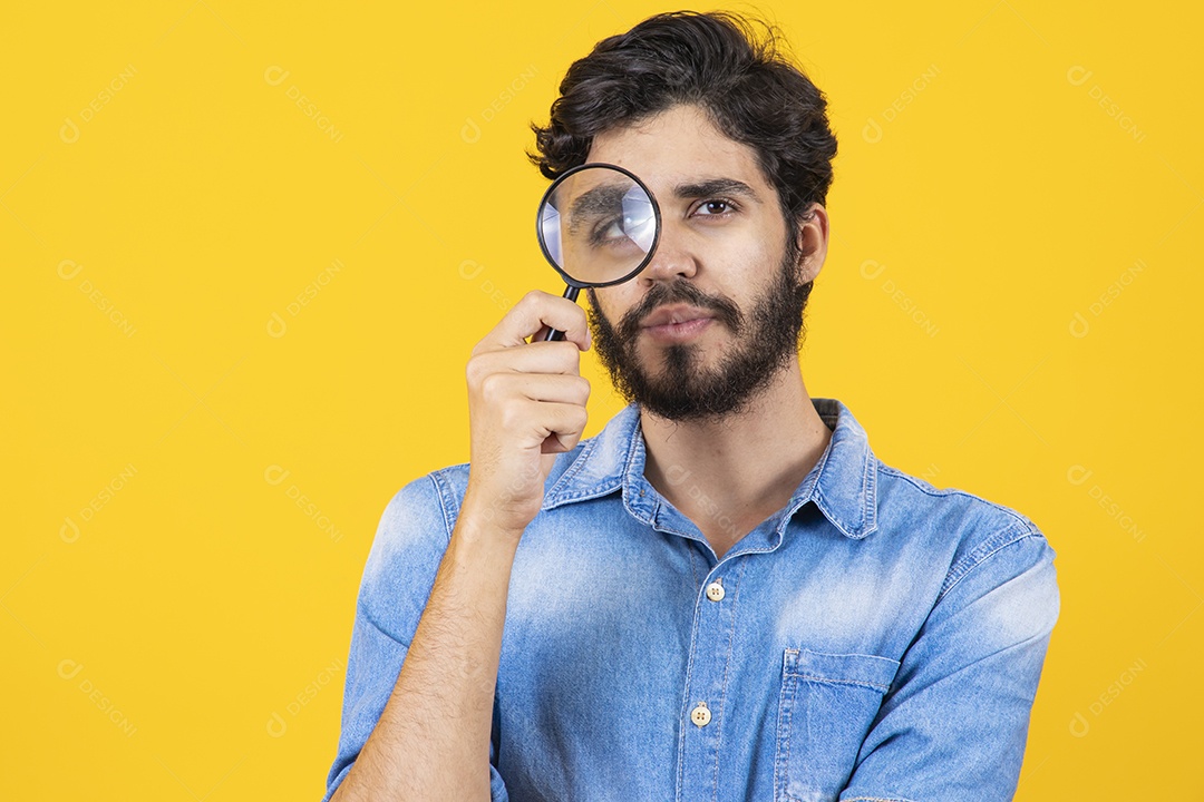 Homem jovem barbudo usando lupa sobre fundo amarelo